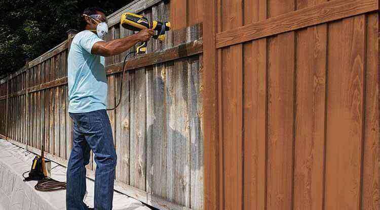 A Man Staining Fence With A Sprayer